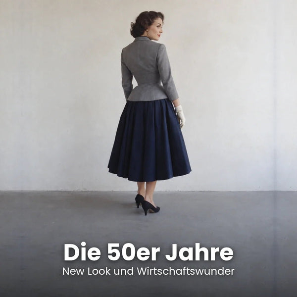 Frau im grauen taillierten Jackett und weiten dunkelblauen Rock im New Look Stil der 1950er Jahre mit weißen Handschuhen