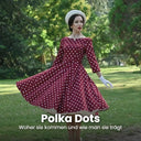 Frau mit weißer Baskenmütze und weißen Handschuhen dreht sich im weinroten Swingkleid mit weißen Polka Dots auf einer Parkwiese