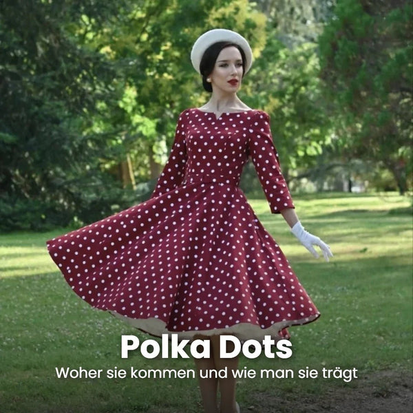 Frau mit weißer Baskenmütze und weißen Handschuhen dreht sich im weinroten Swingkleid mit weißen Polka Dots auf einer Parkwiese